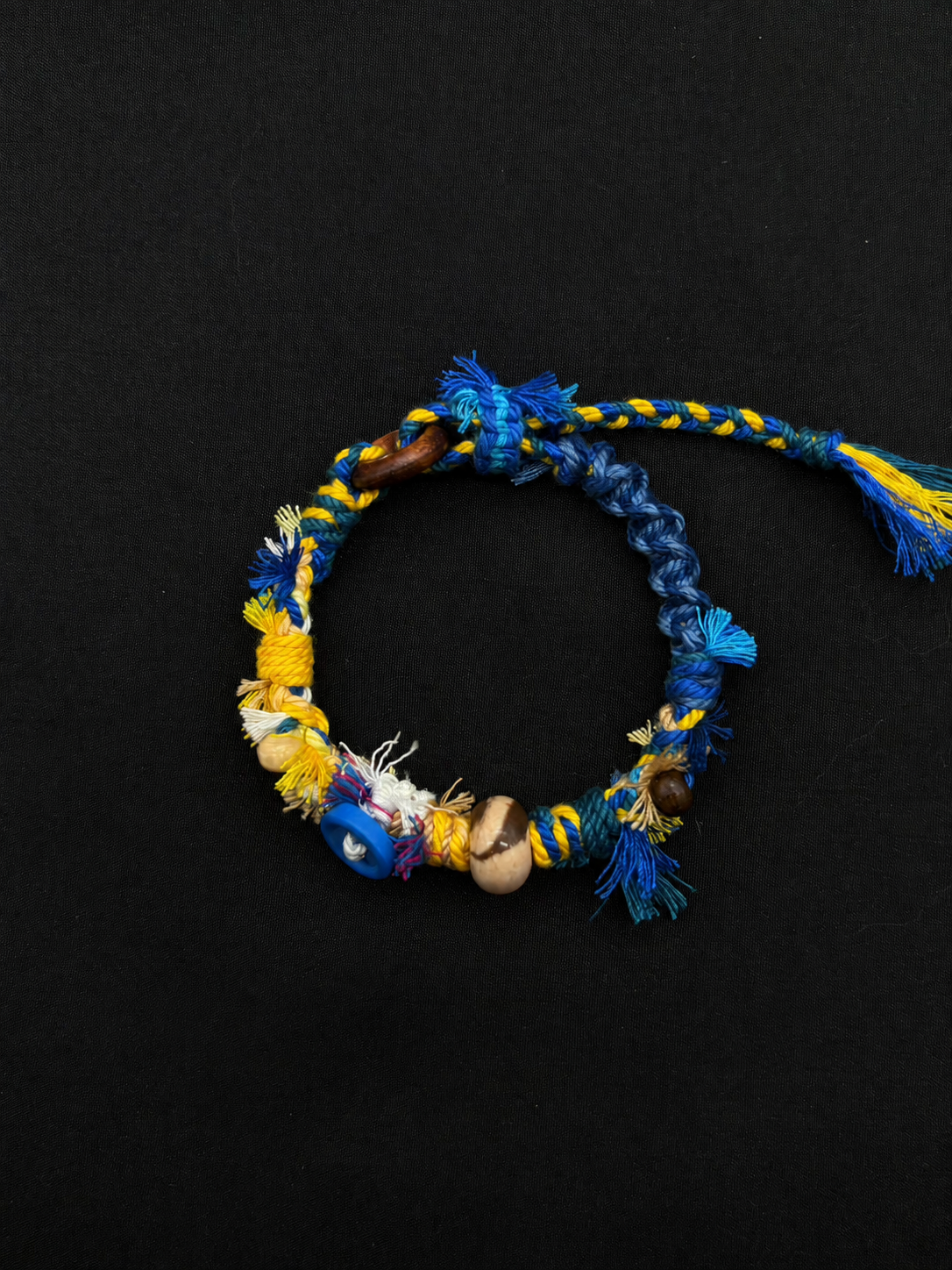Blue Horizon blue and yellow woven bracelet with bright braided cord, a blue disc accent and a two-tone round bead. Product view on dark fabric.