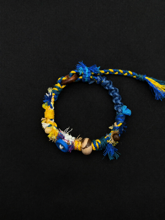 Blue Horizon blue and yellow woven bracelet with bright braided cord, a blue disc accent and a two-tone round bead. Product view on dark fabric.