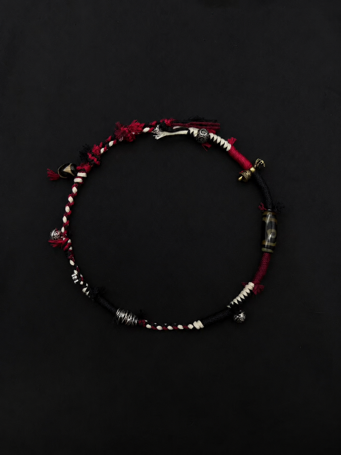 Ember Trail red, black and white woven bracelet with a slender double-wrap design with a patterned tube bead. Product view on dark fabric.